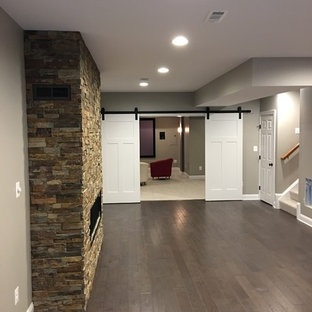 Foto de sótano en el subsuelo actual, grande, con paredes marrones, suelo de madera oscura, chimenea lineal, marco de chimenea de piedra y suelo marrón