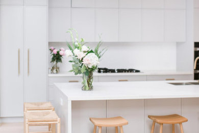 This is an example of a large modern galley eat-in kitchen in Sydney with shaker cabinets, grey cabinets, quartz benchtops, white splashback, engineered quartz splashback, black appliances, with island and white benchtop.
