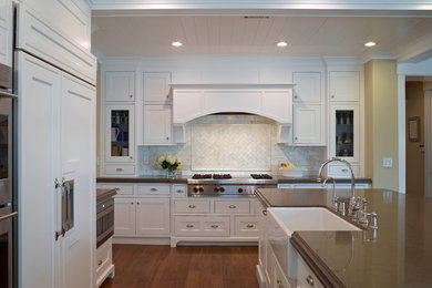 Inspiration for a mid-sized transitional l-shaped medium tone wood floor eat-in kitchen remodel in Other with a farmhouse sink, recessed-panel cabinets, white cabinets, solid surface countertops, white backsplash, stone tile backsplash, stainless steel appliances and an island
