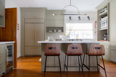 Example of a transitional l-shaped medium tone wood floor and brown floor kitchen design in Toronto with shaker cabinets, gray cabinets, white backsplash, an island and white countertops
