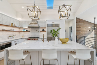 Example of a large transitional l-shaped beige floor kitchen design in San Francisco with a farmhouse sink, shaker cabinets, white cabinets, white backsplash, subway tile backsplash, stainless steel appliances, an island and white countertops
