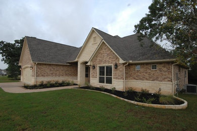 Example of a large classic beige one-story brick house exterior design in Houston with a hip roof and a shingle roof