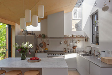 Inspiration for a mid-sized contemporary l-shaped separate kitchen in Other with a double-bowl sink, flat-panel cabinets, grey cabinets, stainless steel benchtops, white splashback, stainless steel appliances, light hardwood floors, with island, beige floor and grey benchtop.