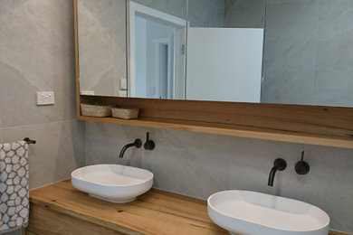 Photo of a large modern wet room bathroom in Melbourne with flat-panel cabinets, medium wood cabinets, a freestanding bath, a one-piece toilet, grey tiles, porcelain tiles, beige walls, porcelain flooring, a vessel sink, wooden worktops, grey floors, an open shower, double sinks and a floating vanity unit.