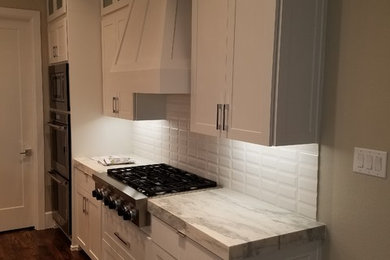 Example of a mid-sized transitional l-shaped brown floor eat-in kitchen design in Dallas with shaker cabinets, white cabinets, marble countertops and an island