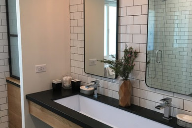 Photo of a mid-sized industrial kids bathroom in Los Angeles with open cabinets, medium wood cabinets, an alcove shower, a one-piece toilet, white tile, subway tile, white walls, a trough sink, granite benchtops, porcelain floors and brown floor.