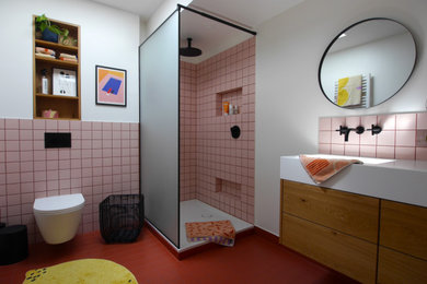 Kleines Nordisches Duschbad mit flächenbündigen Schrankfronten, hellbraunen Holzschränken, offener Dusche, Wandtoilette, rosa Fliesen, weißer Wandfarbe, Zementfliesen für Boden, integriertem Waschbecken, Mineralwerkstoff-Waschtisch, rotem Boden, offener Dusche, Wandnische, Einzelwaschbecken und eingebautem Waschtisch in Dortmund