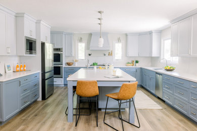 Eat-in kitchen - large transitional u-shaped light wood floor and beige floor eat-in kitchen idea in San Francisco with an undermount sink, shaker cabinets, blue cabinets, quartz countertops, white backsplash, quartz backsplash, stainless steel appliances, an island and white countertops