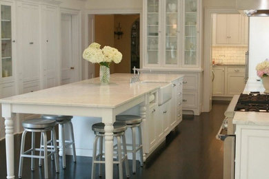 Example of a mid-sized farmhouse u-shaped dark wood floor and brown floor eat-in kitchen design in Other with a farmhouse sink, glass-front cabinets, white cabinets, marble countertops, white backsplash, subway tile backsplash, stainless steel appliances and an island