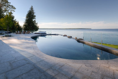 Example of a classic backyard stone and custom-shaped infinity hot tub design in Other