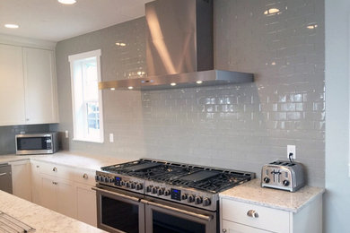 Eat-in kitchen - large contemporary u-shaped medium tone wood floor eat-in kitchen idea in Portland with a double-bowl sink, shaker cabinets, white cabinets, granite countertops, gray backsplash, ceramic backsplash, stainless steel appliances, two islands and white countertops
