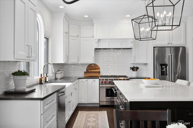 Inspiration for a large transitional l-shaped dark wood floor and brown floor enclosed kitchen remodel in Chicago with a farmhouse sink, shaker cabinets, black cabinets, quartz countertops, white backsplash, subway tile backsplash, stainless steel appliances, an island and black countertops