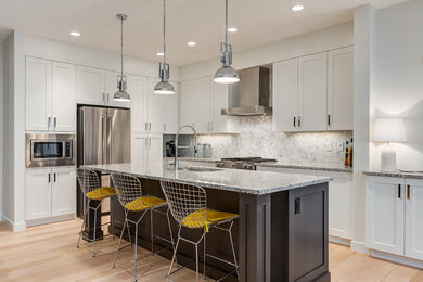 Contemporary kitchen in Calgary with an undermount sink, shaker cabinets, white cabinets, granite benchtops, grey splashback, marble splashback, stainless steel appliances, light hardwood floors, brown floor and grey benchtop.