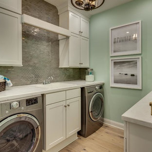 マイアミの中サイズのビーチスタイルのおしゃれなランドリールーム (ドロップインシンク、シェーカースタイル扉のキャビネット、白いキャビネット、緑の壁、淡色無垢フローリング、人工大理石カウンター、左右配置の洗濯機・乾燥機、ベージュの床、白いキッチンカウンター) の写真