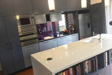 This is an example of a small modern galley open plan kitchen in Sydney with an undermount sink, flat-panel cabinets, blue cabinets, quartzite benchtops, metallic splashback, glass sheet splashback, stainless steel appliances, painted wood floors, with island, orange floor and white benchtop.