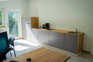 Einzeilige, Mittelgroße Moderne Küche ohne Insel mit Waschbecken, flächenbündigen Schrankfronten, grauen Schränken, Arbeitsplatte aus Holz, Küchenrückwand in Weiß, Elektrogeräten mit Frontblende, hellem Holzboden, grauem Boden und brauner Arbeitsplatte in Sonstige