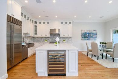 Example of a classic light wood floor kitchen design in New York with white cabinets, marble backsplash, an island and white countertops