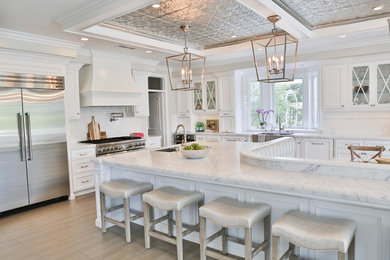 Inspiration for a large transitional l-shaped porcelain tile and gray floor eat-in kitchen remodel in San Diego with a farmhouse sink, raised-panel cabinets, white cabinets, marble countertops, white backsplash, marble backsplash, stainless steel appliances and an island