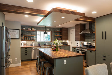 Large mountain style u-shaped medium tone wood floor, brown floor and exposed beam eat-in kitchen photo in Denver with a farmhouse sink, flat-panel cabinets, green cabinets, wood countertops, gray backsplash, subway tile backsplash, stainless steel appliances, an island and brown countertops