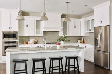 Inspiration for a mid-sized transitional l-shaped dark wood floor and brown floor open concept kitchen remodel in Minneapolis with a farmhouse sink, shaker cabinets, white cabinets, quartz countertops, gray backsplash, subway tile backsplash, stainless steel appliances and an island
