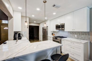 Inspiration for a mid-sized transitional laminate floor and gray floor kitchen remodel in Houston with a farmhouse sink, shaker cabinets, white cabinets, quartz countertops, gray backsplash, porcelain backsplash, stainless steel appliances and white countertops