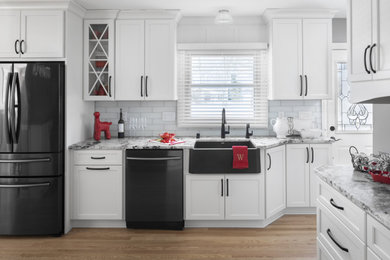 Photo of a mid-sized contemporary u-shaped eat-in kitchen in Milwaukee with a farmhouse sink, recessed-panel cabinets, white cabinets, granite benchtops, white splashback, glass tile splashback, black appliances, light hardwood floors, beige floor and white benchtop.
