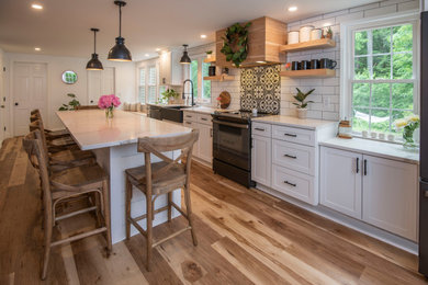 Inspiration for a mid-sized farmhouse eat-in kitchen remodel in Boston with a farmhouse sink, shaker cabinets, white cabinets, quartz countertops, white backsplash, subway tile backsplash, black appliances, an island and white countertops