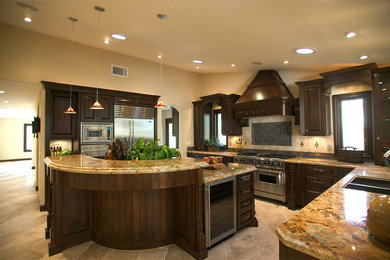 Example of a huge classic u-shaped travertine floor and beige floor kitchen pantry design in Los Angeles with an undermount sink, raised-panel cabinets, dark wood cabinets, granite countertops, beige backsplash, porcelain backsplash, stainless steel appliances and an island