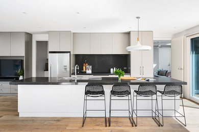 Contemporary galley kitchen in Melbourne with a drop-in sink, flat-panel cabinets, grey cabinets, stainless steel appliances, medium hardwood floors, with island, brown floor and black benchtop.