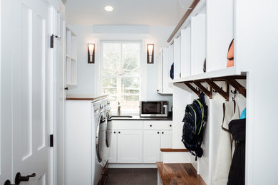 Mid-sized elegant l-shaped porcelain tile and brown floor utility room photo in Burlington with an undermount sink, shaker cabinets, white cabinets, soapstone countertops, blue walls, a side-by-side washer/dryer and black countertops