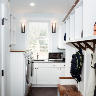バーリントンの中サイズのトラディショナルスタイルのおしゃれな家事室 (アンダーカウンターシンク、シェーカースタイル扉のキャビネット、白いキャビネット、ソープストーンカウンター、青い壁、磁器タイルの床、左右配置の洗濯機・乾燥機、茶色い床、黒いキッチンカウンター) の写真