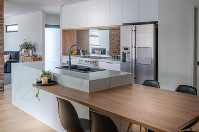 Inspiration for a large modern galley light wood floor open concept kitchen remodel in San Francisco with a double-bowl sink, flat-panel cabinets, white cabinets, quartz countertops, brick backsplash, stainless steel appliances, an island and white countertops