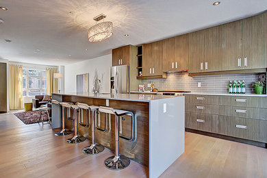Example of a mid-sized transitional single-wall light wood floor kitchen design in Calgary with flat-panel cabinets, medium tone wood cabinets, solid surface countertops, gray backsplash, porcelain backsplash, stainless steel appliances and an island
