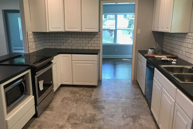 Mid-sized elegant l-shaped linoleum floor and gray floor eat-in kitchen photo in Houston with a double-bowl sink, shaker cabinets, white cabinets, laminate countertops, white backsplash, subway tile backsplash, stainless steel appliances and black countertops