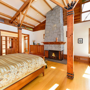 Inredning av ett maritimt sovrum, med vita väggar, mellanmörkt trägolv, en standard öppen spis och en spiselkrans i sten