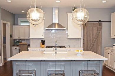 This is an example of a large transitional eat-in kitchen in Omaha with a farmhouse sink, shaker cabinets, white cabinets, quartz benchtops, white splashback, glass tile splashback, stainless steel appliances, medium hardwood floors and with island.