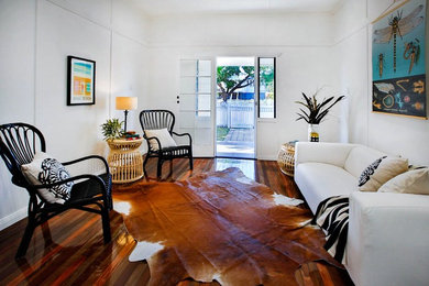 Mid-sized tropical living room in Townsville with white walls and medium hardwood floors.