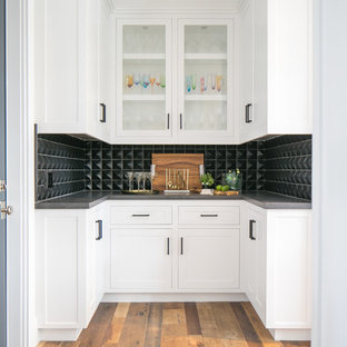 オレンジカウンティのビーチスタイルのおしゃれなホームバー (シンクなし、シェーカースタイル扉のキャビネット、白いキャビネット、黒いキッチンパネル、無垢フローリング、茶色い床) の写真