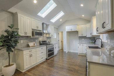Inspiration for a timeless dark wood floor and brown floor kitchen remodel in Kansas City with white cabinets, quartz countertops, gray backsplash, travertine backsplash, stainless steel appliances and gray countertops
