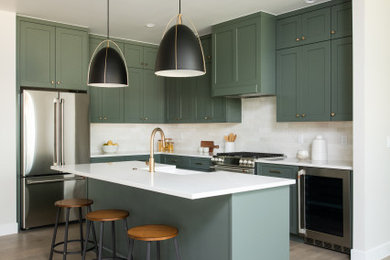 Eat-in kitchen - transitional l-shaped medium tone wood floor eat-in kitchen idea in Denver with a farmhouse sink, shaker cabinets, green cabinets, quartz countertops, white backsplash, ceramic backsplash, stainless steel appliances, an island and white countertops