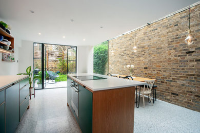 Design ideas for a large contemporary galley kitchen/diner in London with a single-bowl sink, flat-panel cabinets, green cabinets, composite countertops, white splashback, black appliances, terrazzo flooring, an island, grey floors and white worktops.