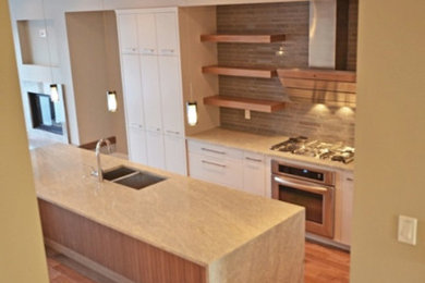 Trendy single-wall medium tone wood floor and brown floor open concept kitchen photo in Calgary with a double-bowl sink, flat-panel cabinets, white cabinets, granite countertops, gray backsplash, stone tile backsplash, an island and stainless steel appliances