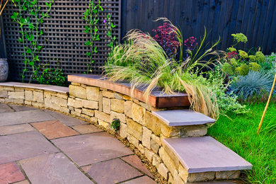 Design ideas for a small modern back xeriscape full sun garden for summer in Surrey with a retaining wall, natural stone paving and a wood fence.