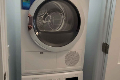 Small trendy porcelain tile and white floor dedicated laundry room photo in Chicago with flat-panel cabinets, white walls and a stacked washer/dryer