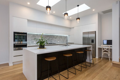 Design ideas for a large contemporary galley open plan kitchen in Auckland with an undermount sink, flat-panel cabinets, white cabinets, quartz benchtops, metallic splashback, ceramic splashback, stainless steel appliances, light hardwood floors, with island and brown floor.