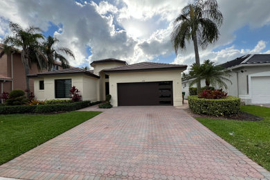 Large minimalist beige one-story stucco and board and batten house exterior photo in Miami with a butterfly roof, a tile roof and a brown roof