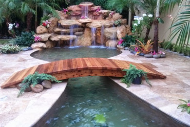Photo of a large tropical backyard partial sun garden in Miami with with pond and natural stone pavers.