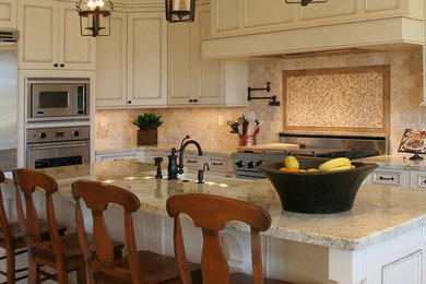 Inspiration for a mid-sized timeless l-shaped brown floor kitchen remodel in Phoenix with a farmhouse sink, recessed-panel cabinets, white cabinets, granite countertops, beige backsplash, stone tile backsplash, stainless steel appliances and an island