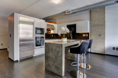 Small trendy l-shaped dark wood floor open concept kitchen photo in Boise with an undermount sink, flat-panel cabinets, quartz countertops, black backsplash, stainless steel appliances, white cabinets, stone tile backsplash and an island