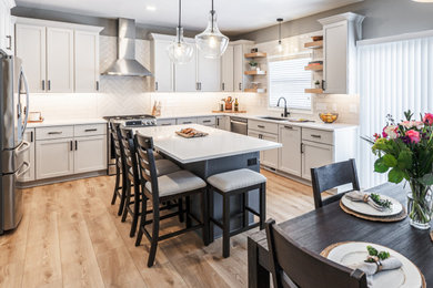 Open concept kitchen - large transitional u-shaped medium tone wood floor and brown floor open concept kitchen idea with a drop-in sink, shaker cabinets, gray cabinets, quartz countertops, beige backsplash, ceramic backsplash, stainless steel appliances, an island and white countertops
